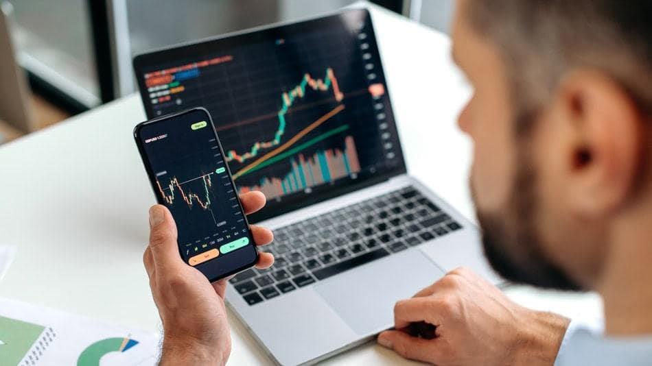 تصویر فردی که تلفن و لپتاپ در دست داشته و در حال بررسی نمودار است.